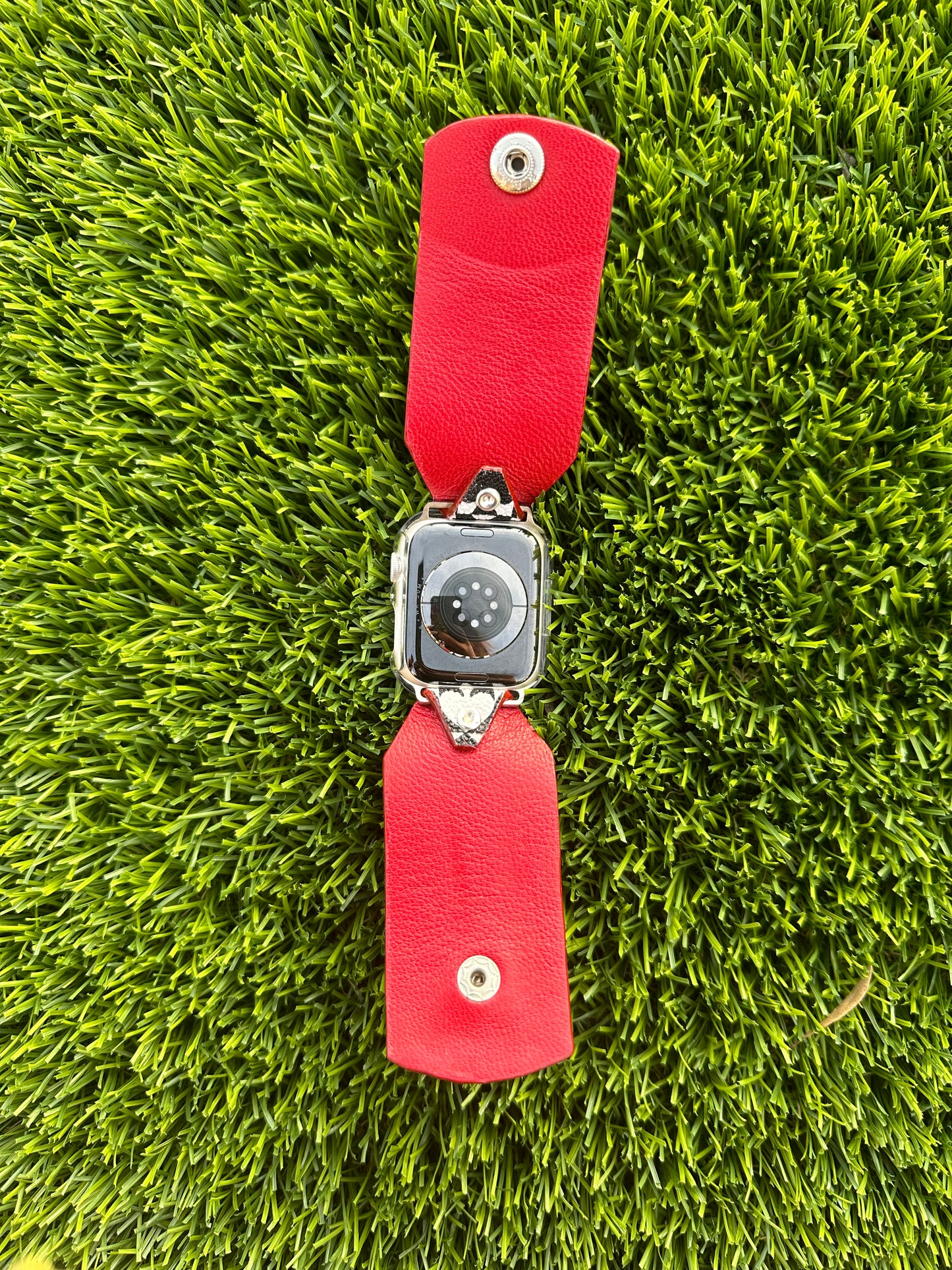 An upcycled Kate Spade band. This band is made from a PVC coated canvas. The design consists of an alternating black and white pattern with a red leather lining and matching edge paint. The band is embellished with a red silver rimmed crystal with matching hardware.