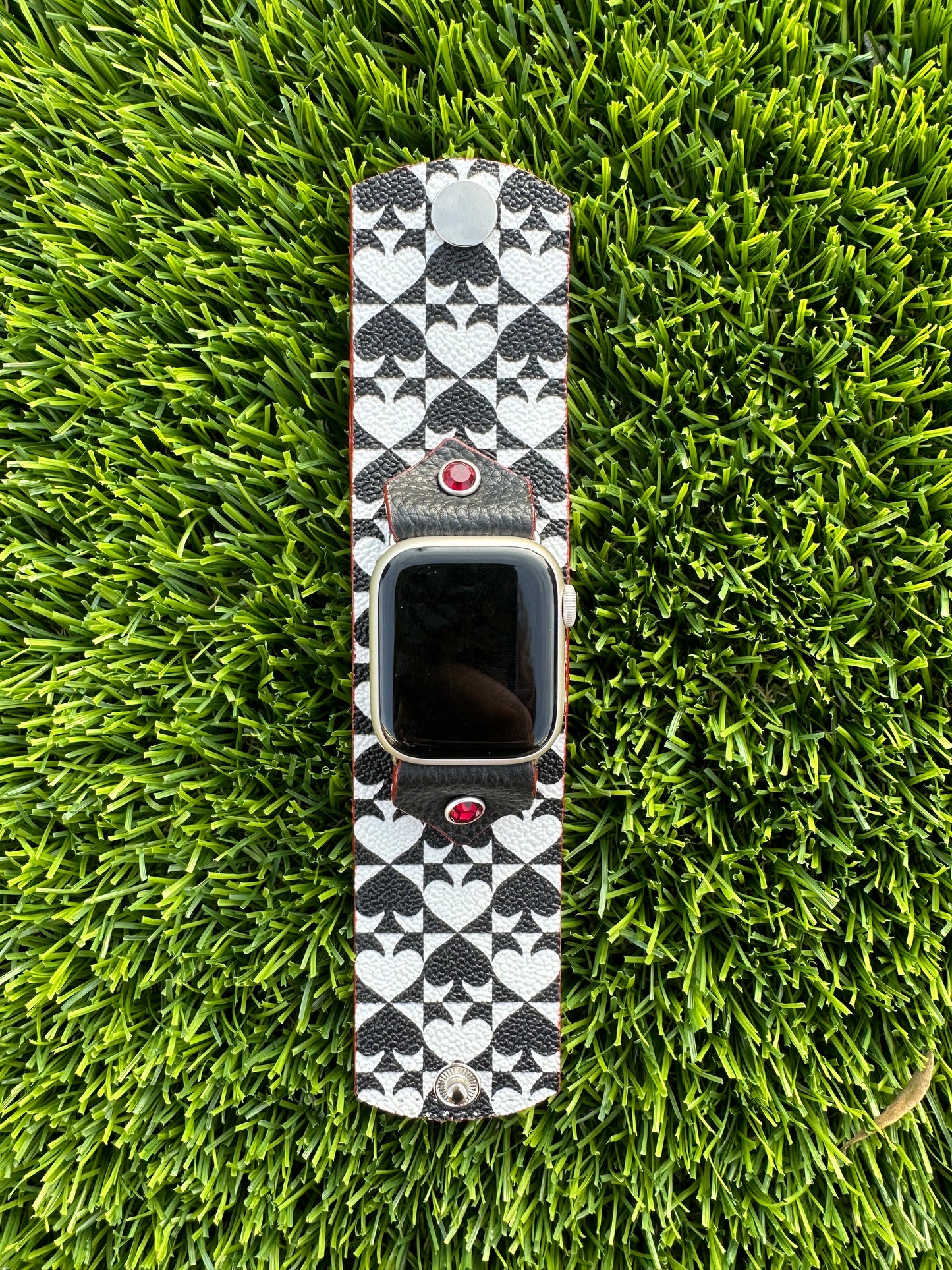An upcycled Kate Spade band. This band is made from a PVC coated canvas. The design consists of an alternating black and white pattern with a red leather lining and matching edge paint. The band is embellished with a red silver rimmed crystal with matching hardware.