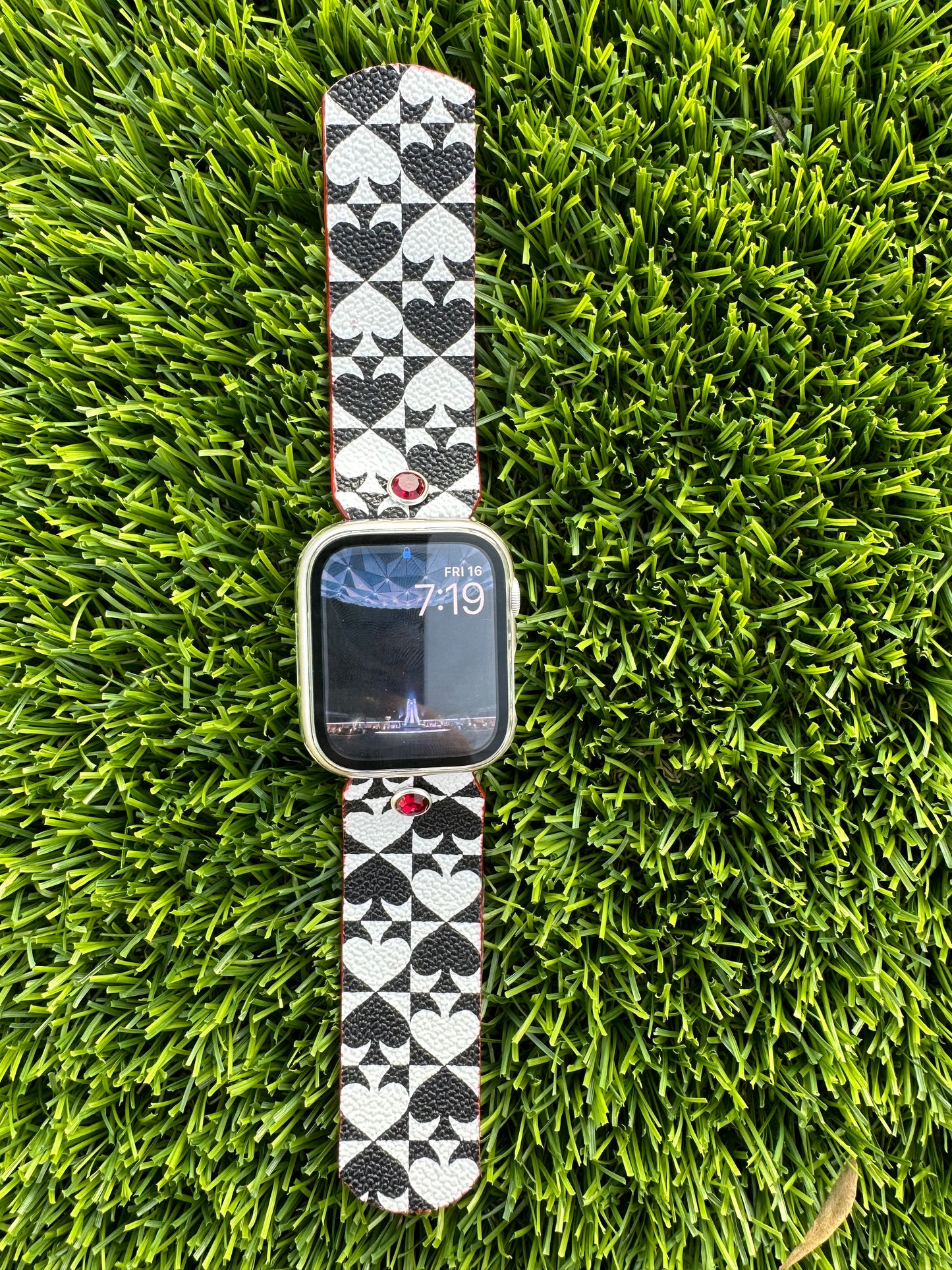 An upcycled Kate Spade band. This band is made from a PVC coated canvas. The design consists of an alternating black and white pattern with a red leather lining and matching edge paint. The band is embellished with a red silver rimmed crystal with matching hardware.