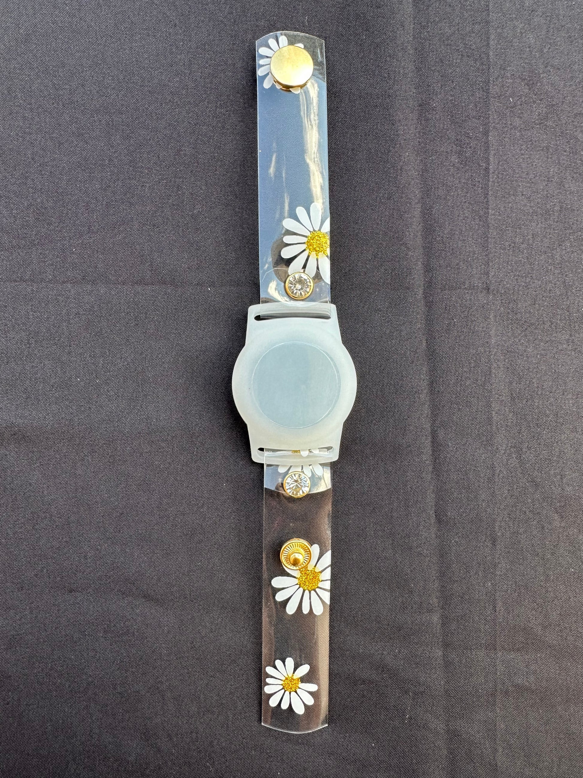 Anya style transparent PVC waterproof band perfect for all year round. The band has scattered daisies with a glittery gold center. The design is embellished with clear crystals with a gold rim. Frosted White Air Tag holder will act as the band's center. 