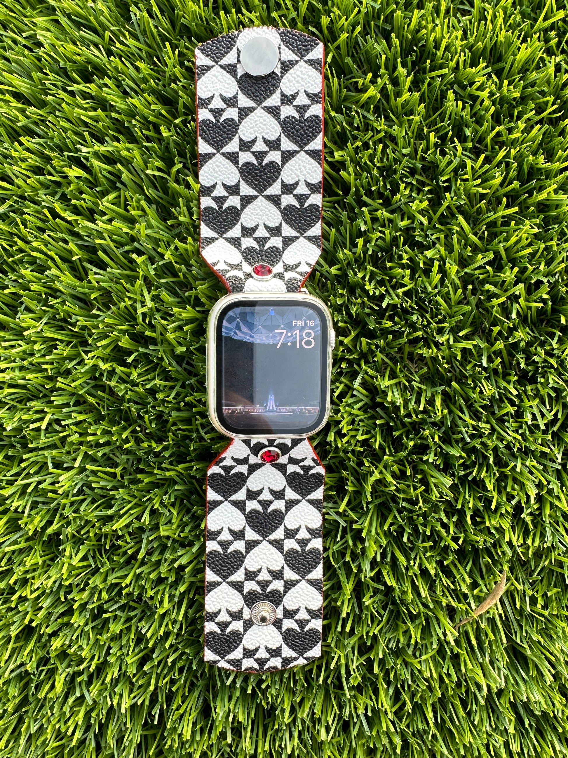 An upcycled Kate Spade band. This band is made from a PVC coated canvas. The design consists of an alternating black and white pattern with a red leather lining and matching edge paint. The band is embellished with a red silver rimmed crystal with matching hardware. 