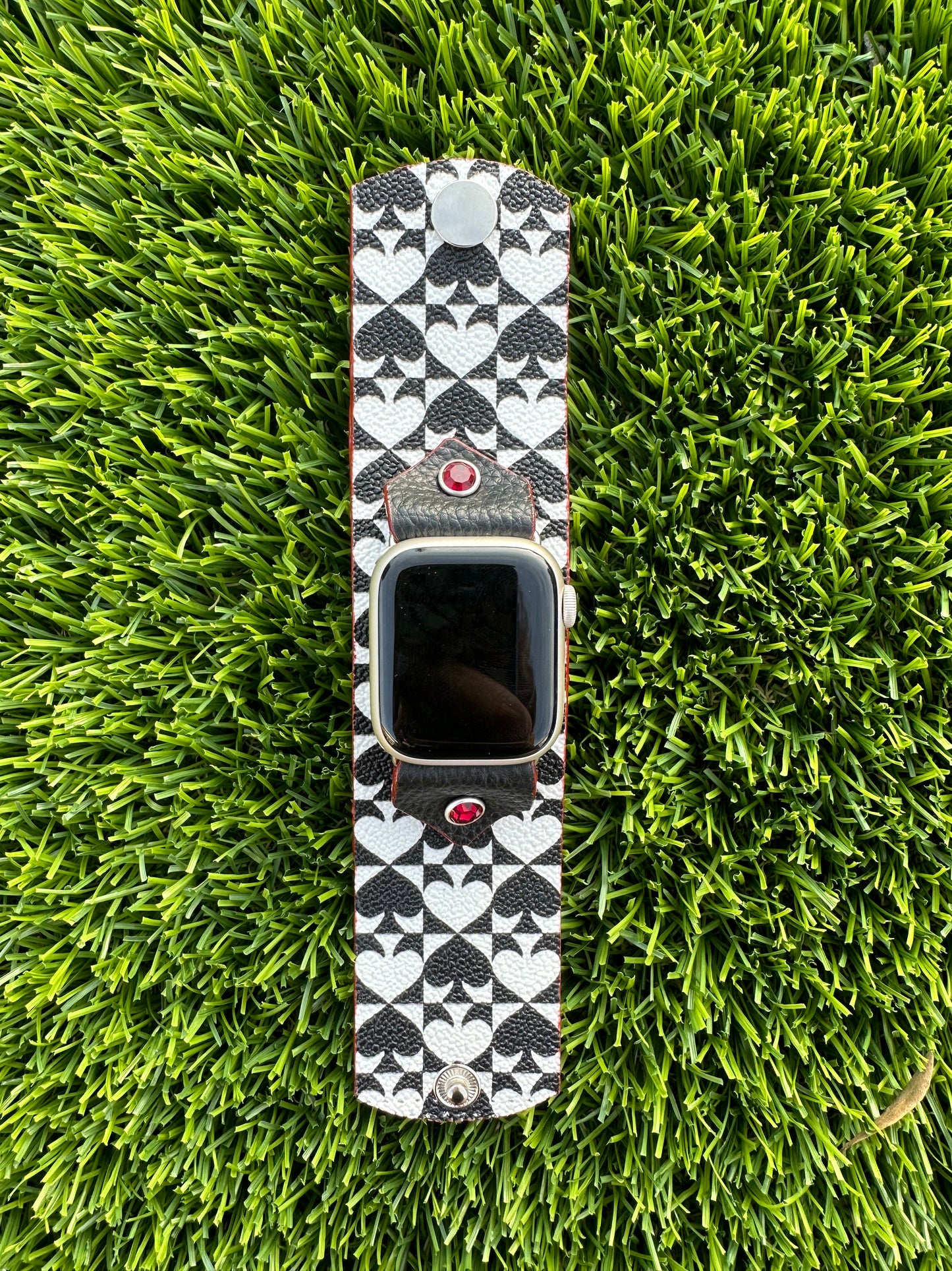 An upcycled Kate Spade band. This band is made from a PVC coated canvas. The design consists of an alternating black and white pattern with a red leather lining and matching edge paint. The band is embellished with a red silver rimmed crystal with matching hardware. 