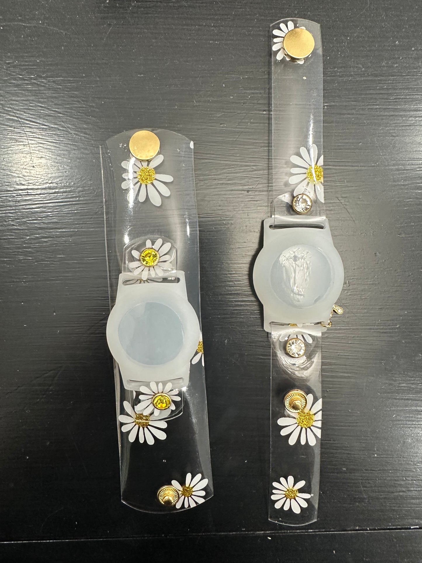 Anya style transparent PVC waterproof band perfect for all year round. The band has scattered daisies with a glittery gold center. The design is embellished with clear crystals with a gold rim. Frosted White Air Tag holder will act as the band's center. 