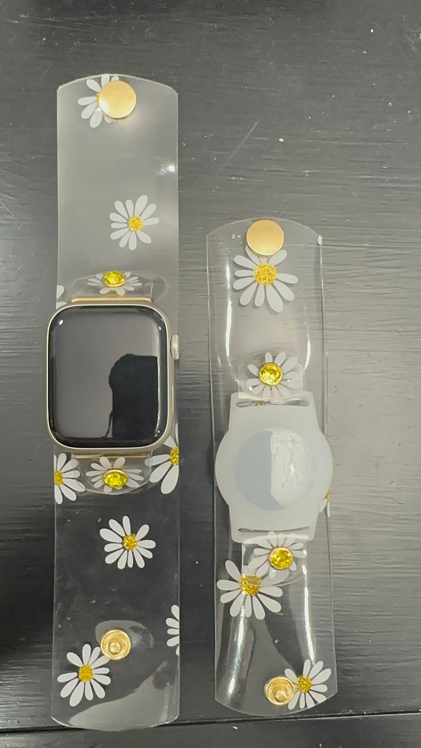 Anya style transparent PVC waterproof band perfect for all year round. The band has scattered daisies with a glittery gold center. The design is embellished with clear crystals with a gold rim. Frosted White Air Tag holder will act as the band's center. 