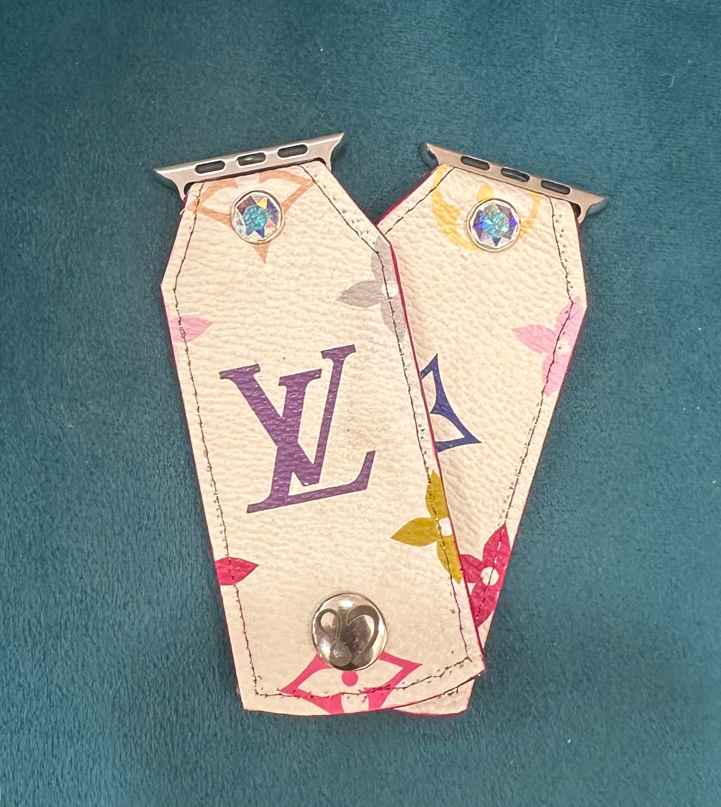 This is an authentic upcycled white mutlicolor LV band. A leather material with the classic LV monogram in multicolors on a white background. It is paired with silver rimmed clear crystal and matching hardware.